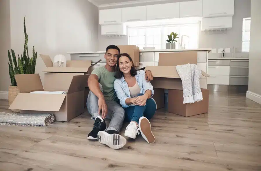 A couple sitting amid boxes on the floor of their new home.